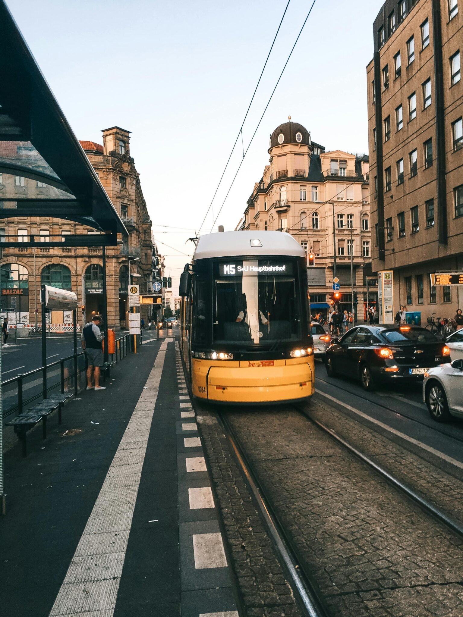 A bustling Berlin street with a yellow tram and historic buildings under a warm sunset glow.